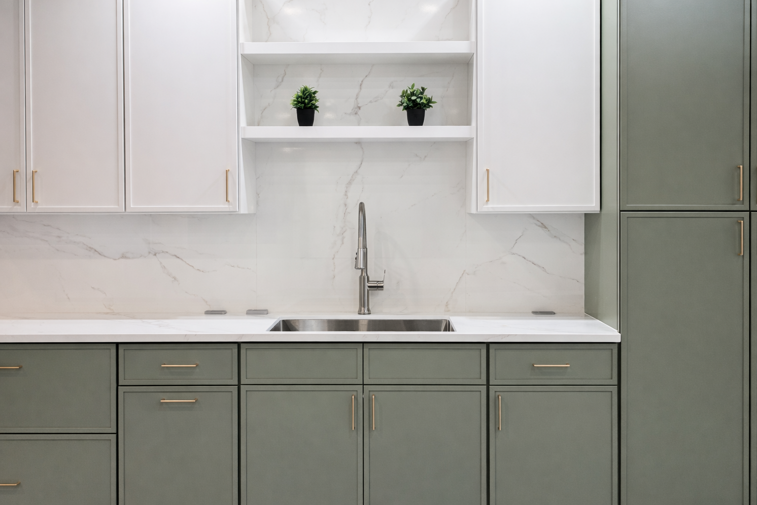Clean kitchen with white upper slim shaker cabinets, green lower slim shaker cabinets, white floating shelves, gold hardware, white quartz countertops and backsplash, stainless steel undermount sink, and modern pull-down faucet.